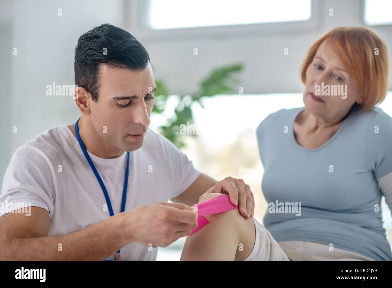 Abile terapista maschile che mette una speciale fascia sul ginocchio Foto Stock