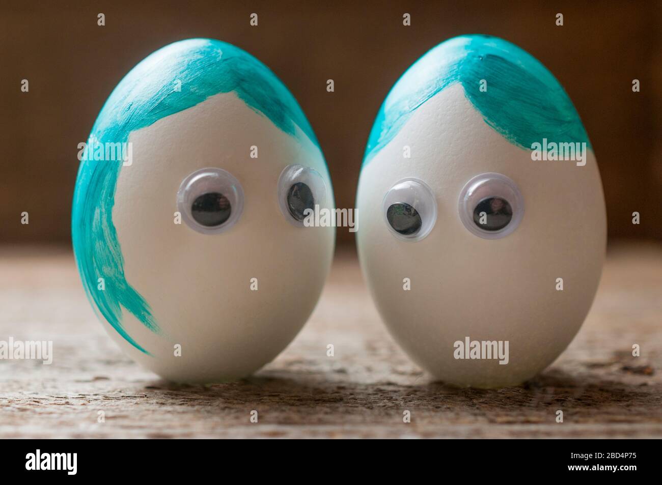 Due uova di pasqua bianche con capelli dipinti e occhi di plastica che parlano l'uno con l'altro su un pavimento in legno Foto Stock
