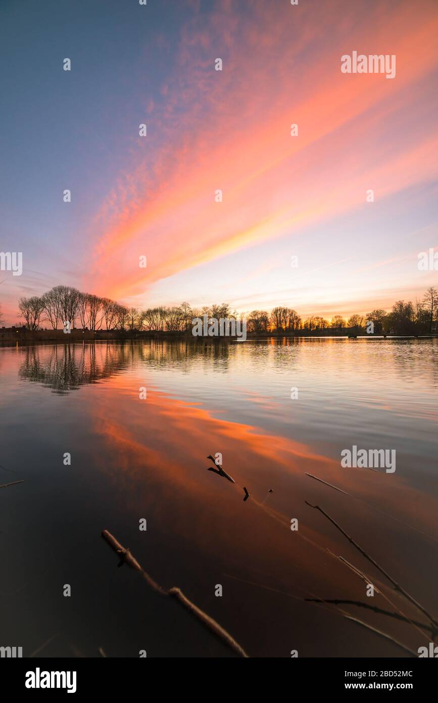 Le nuvole sono illuminate colorosamente dalla luce del sole che tramonta. Bei riflessi nelle acque calme del lago. Foto Stock