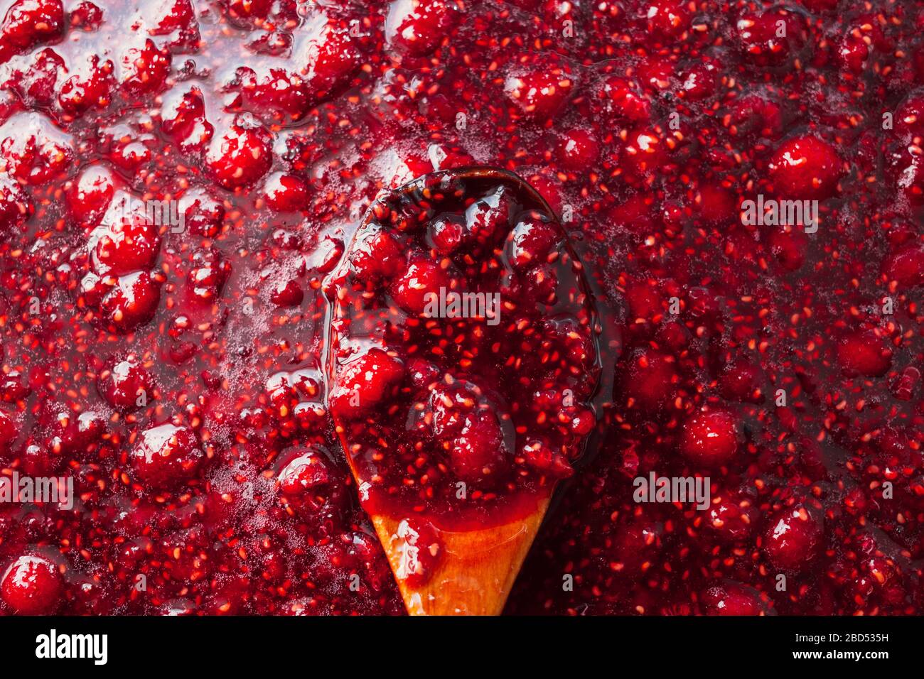 la marmellata di lamponi viene conservata con un cucchiaio di legno Foto Stock