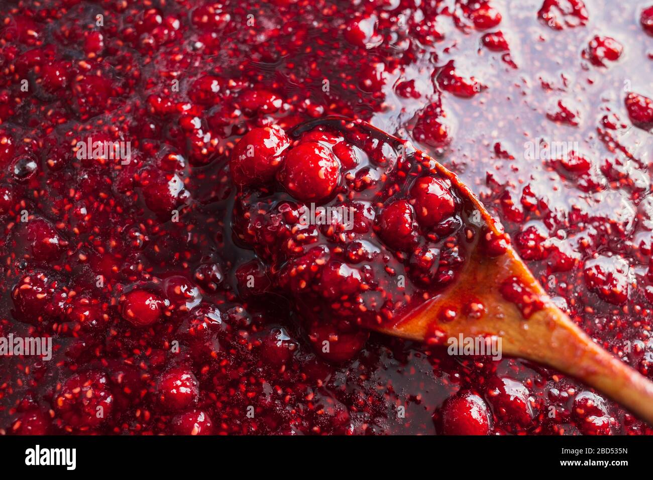 la marmellata di lamponi viene agitata con un cucchiaio di legno. Foto Stock