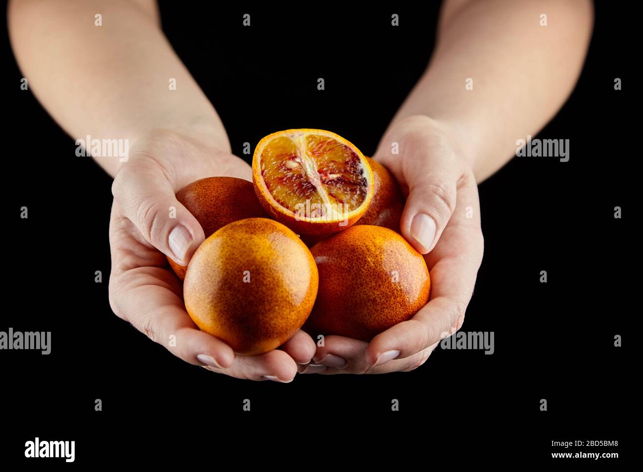 Arance rosse o sanguigne in mano su sfondo nero. Persona che bufing manciata di arance intere e dimezzate. Mucchio di agrumi non sbucciati, fuoco selettivo Foto Stock