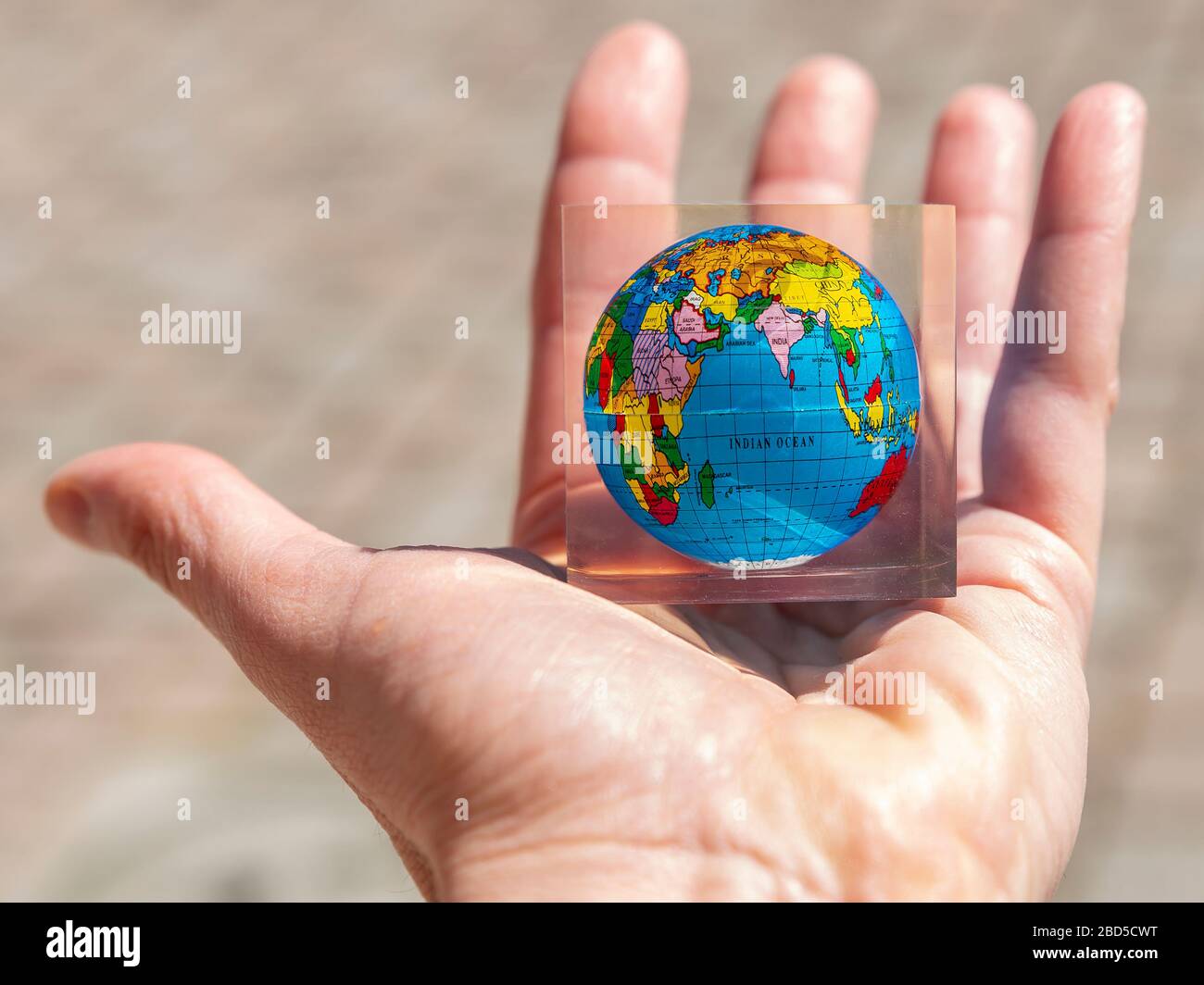 Una mano maschile tiene un pianeta terra colorato nel palmo con una mappa in una cornice di vetro trasparente Foto Stock
