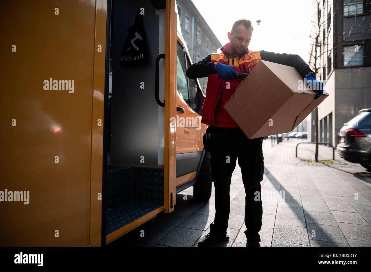 Gelsenkirchen, Germania. 7 aprile 2020. Nino Molldmann, il servizio di consegna pacchi di DHL, carica i pacchi dalla sua auto e li scansiona. È uno degli "eroi della crisi corona" e lavora in una professione di importanza sistemica. Credit: Fabian Strauch/dpa/Alamy Live News Foto Stock