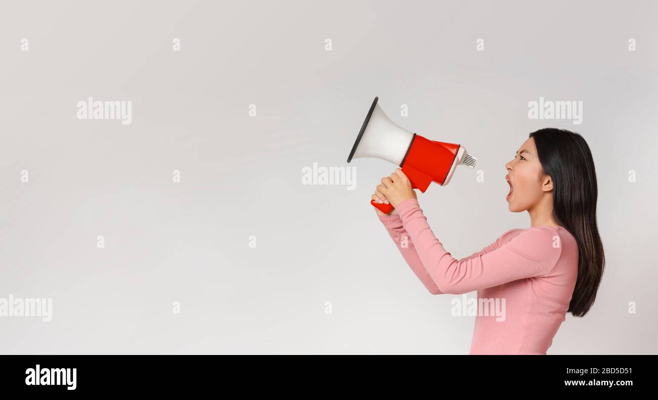 Donna asiatica arrabbiata che gridava in megaphone su sfondo grigio Foto Stock
