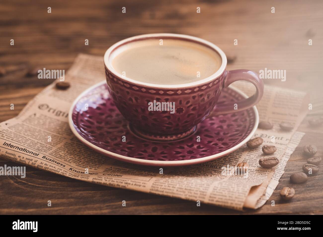 Bella tazza di caffè viola con fagioli sullo sfondo del giornale, fuoco selettivo, annata tonata Foto Stock