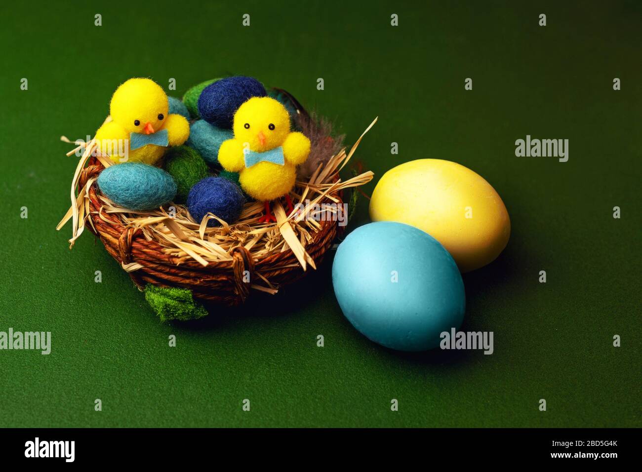 Uova di pasqua in gesso colorato su sfondo verde con cesto e giocattoli di pollo. Foto Stock