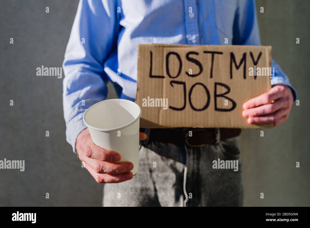 Uomo lavoratore in ufficio in camicia blu con segno di cartone PERSO LAVORO. Senza lavoro, concetto di disoccupazione. Chiedere soldi con tazza di carta Foto Stock