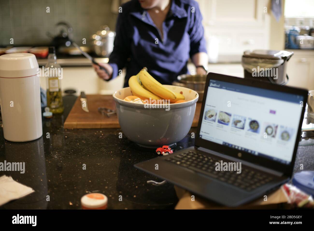 La madre prepara la cena di famiglia a casa mentre lavora su un computer portatile in cucina durante l'autoisolamento durante la pandemia di coronavirus 2020 COVID-19 Foto Stock