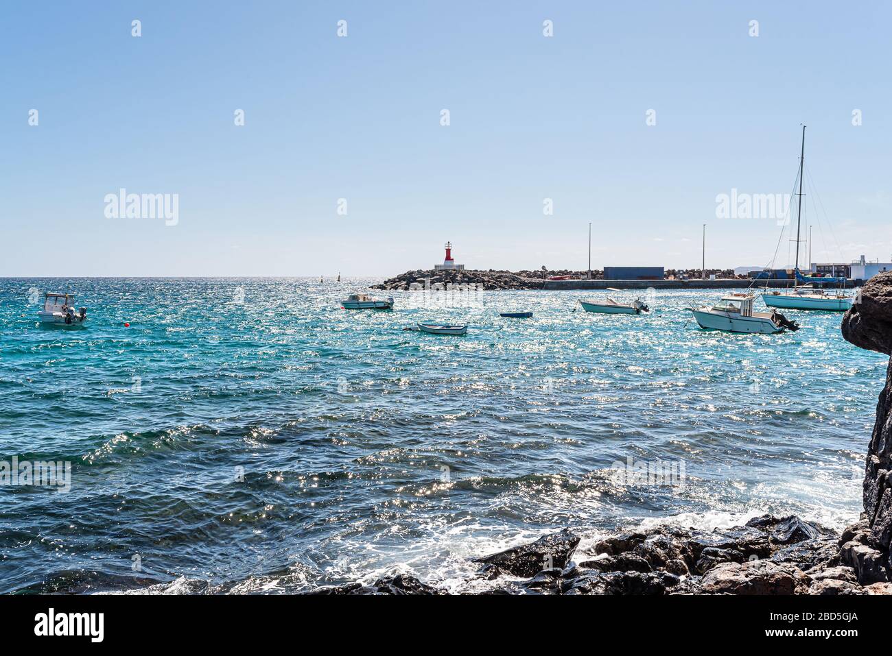 Piccole barche sull'oceano vicino a Playa Blanca, terminal dei traghetti di Lanzarote contro il cielo blu brillante Foto Stock