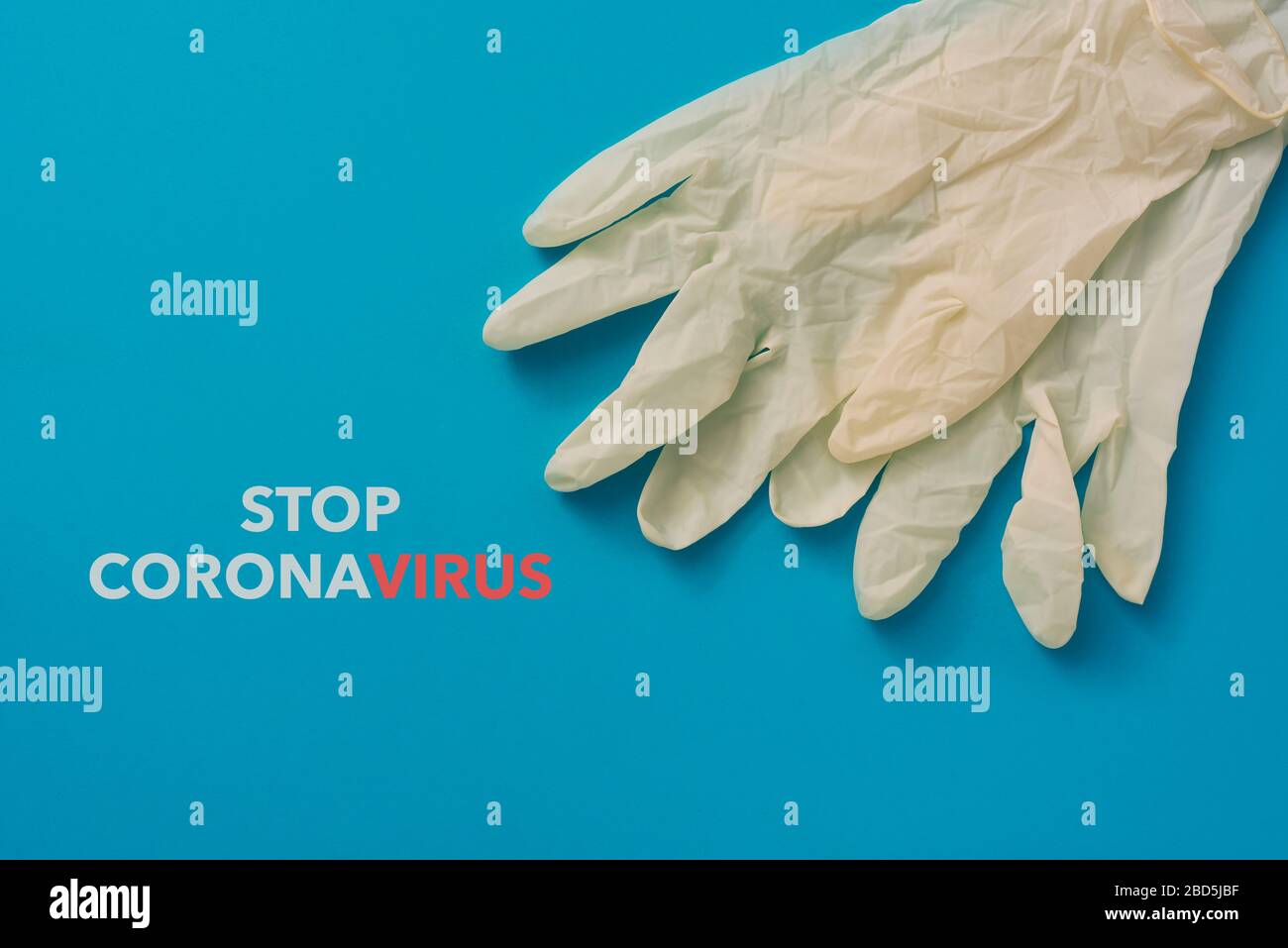 vista ad angolo elevato di un paio di guanti chirurgici monouso e del coronavirus di arresto del testo su uno sfondo blu Foto Stock