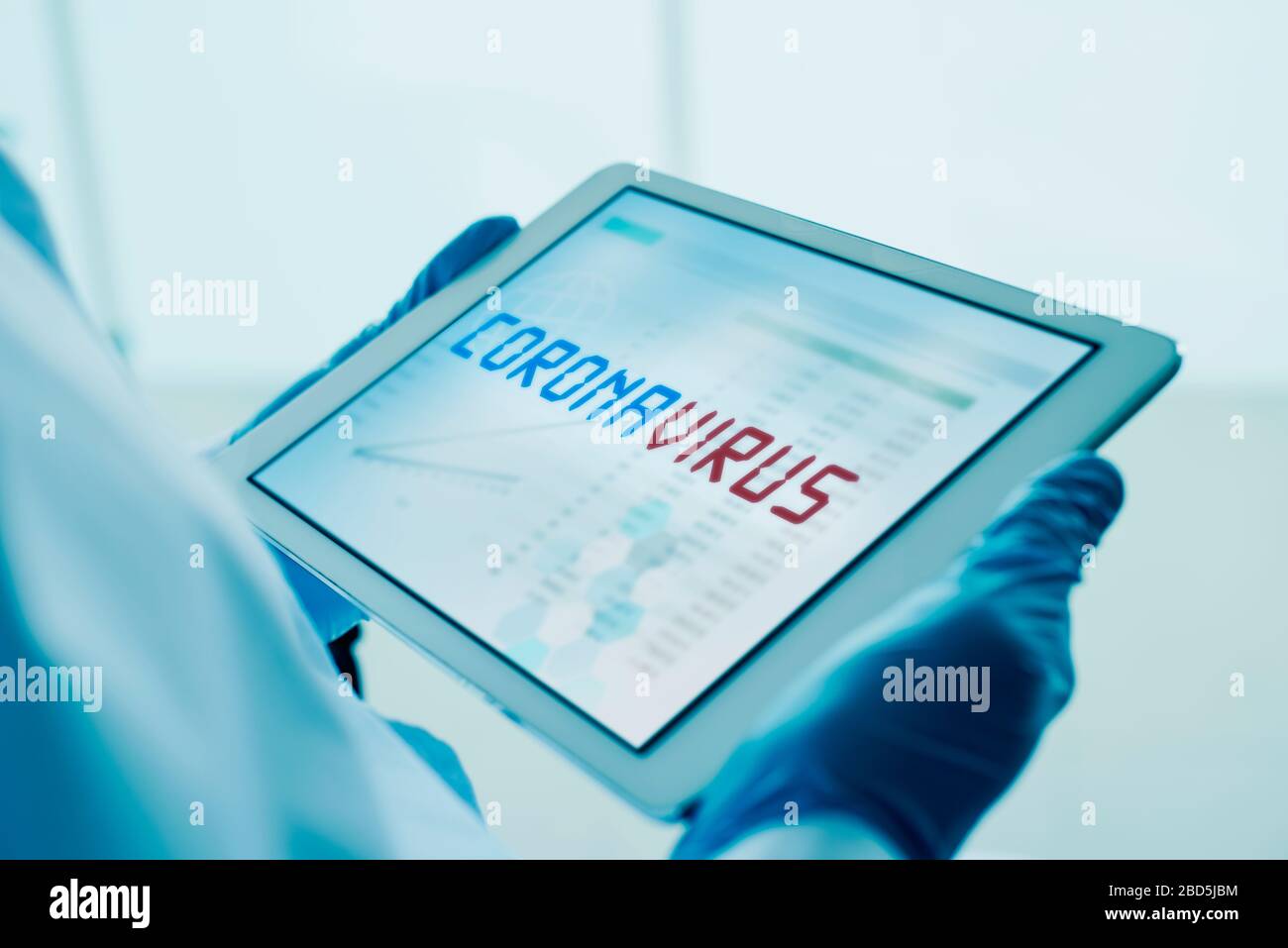 primo piano di un medico uomo, indossando guanti chirurgici blu, avendo una tavoletta digitale nelle sue mani con il testo coronavirus nel suo schermo Foto Stock