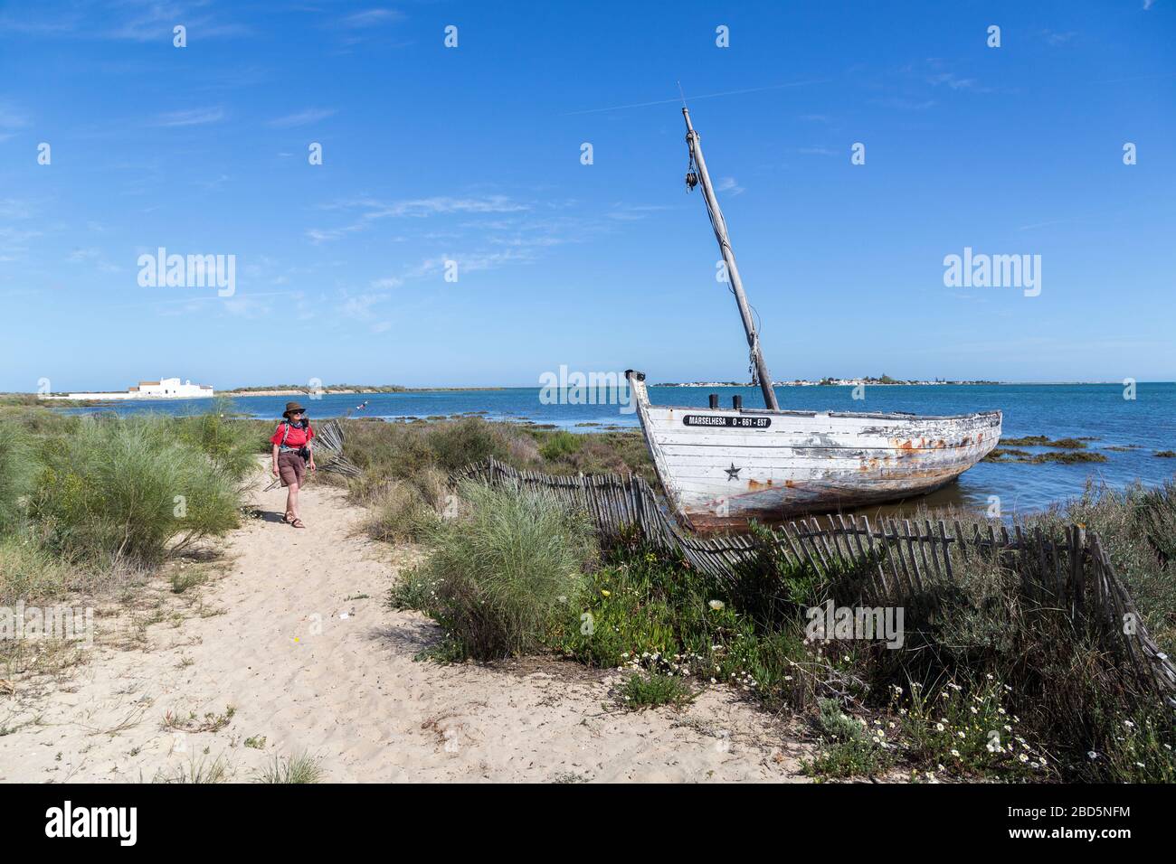 Vecchia barca abbandonata in baracche con camminatore sul sentiero costiero, Quinta de Marim, Parco Naturale Ria Formosa, Algarve, Portogallo Foto Stock