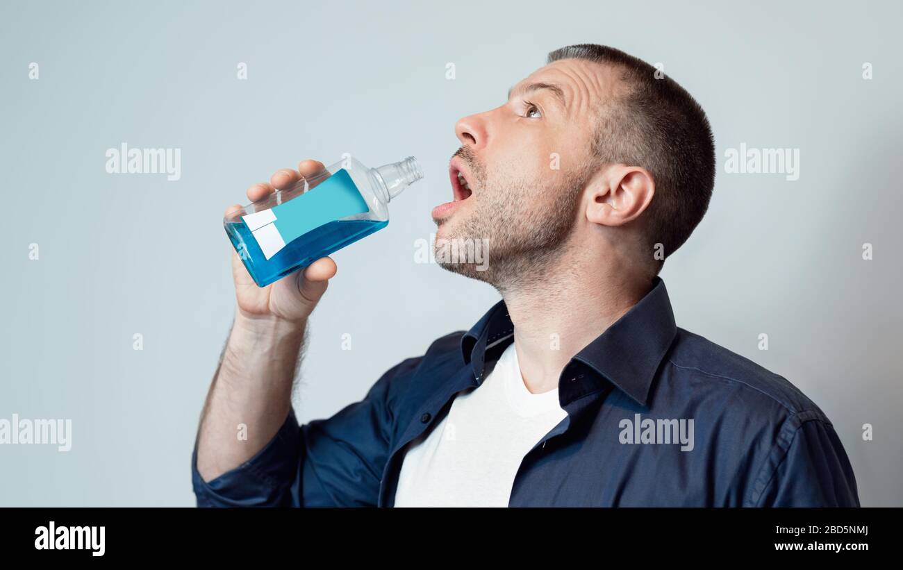 Uomo bocca di lavaggio con risciacquo orale in piedi su sfondo grigio Foto Stock