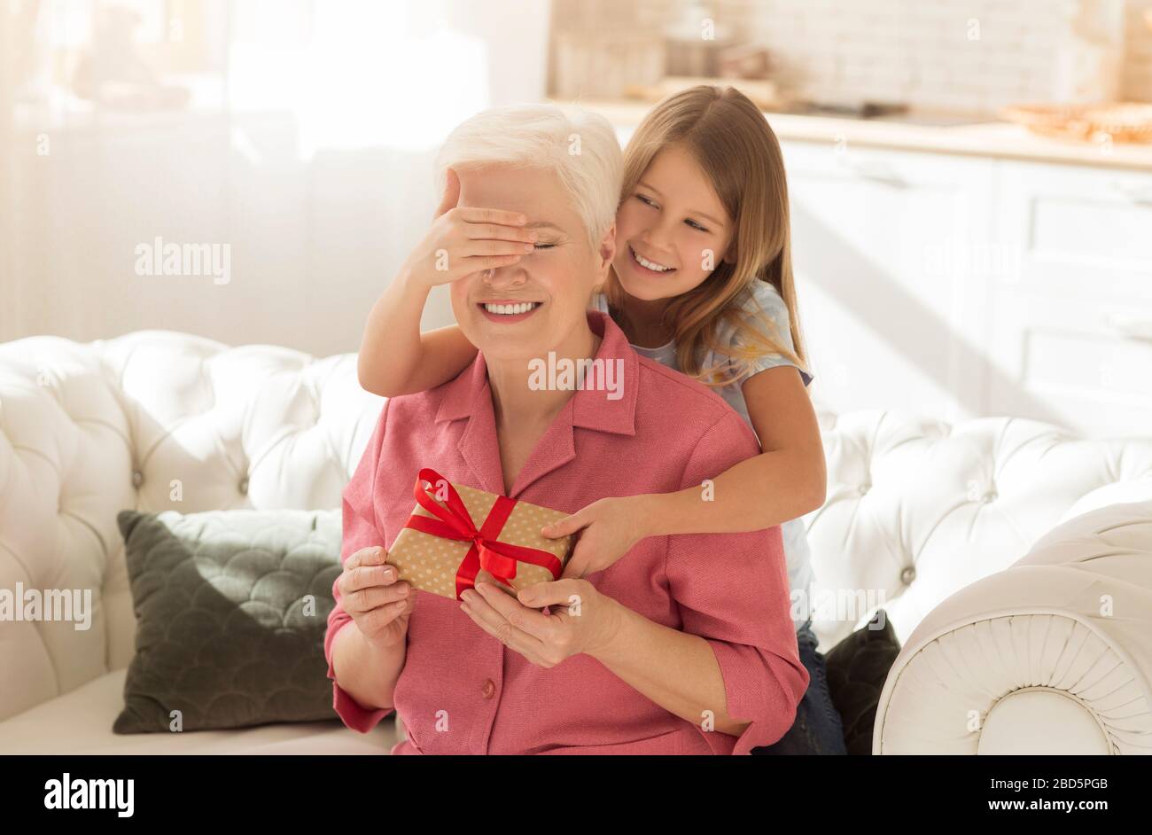 Bambino cute che chiude gli occhi della sua nonna mentre dà presente a casa Foto Stock