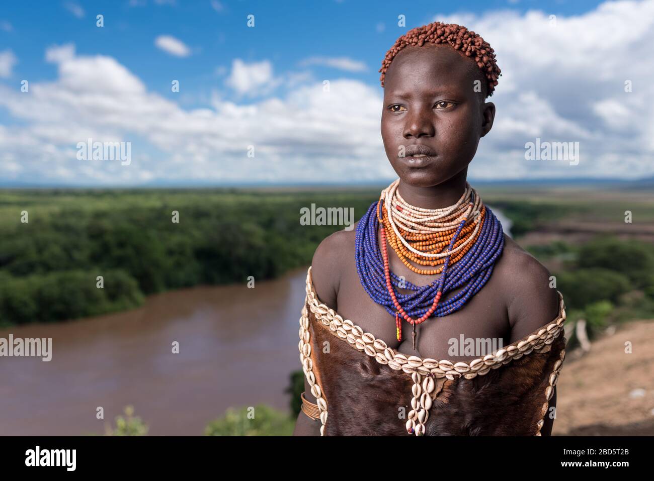 Sopra il fiume Omo, una tribù di Karo o membro del gruppo etnico indossa i suoi migliori perline e abito di pelle di capra, i suoi capelli intrecciati con argilla, Tumi, Etiopia. Foto Stock