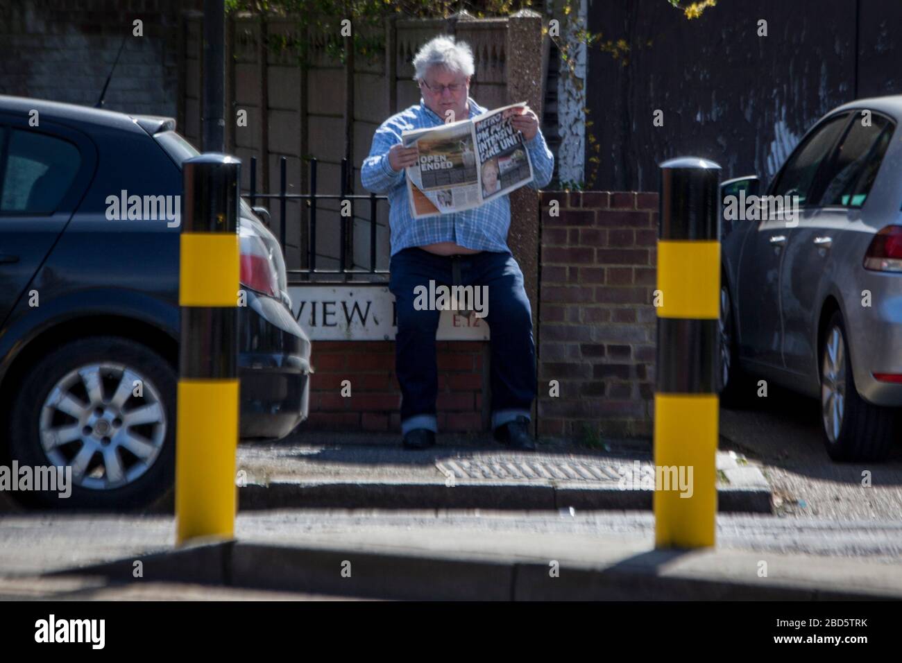 Manor Park, Londra, Regno Unito. 7 aprile 2020. Un uomo legge un giornale che il titolo dice: 'PM messo a unità di cura intesive', vicino al morgue.Works sulla costruzione di un morgue temporaneo a Manor Park, Londra est continua; a causa di focolaio di coronavirus. Credit: Marcin Nowak/Alamy Live News Foto Stock