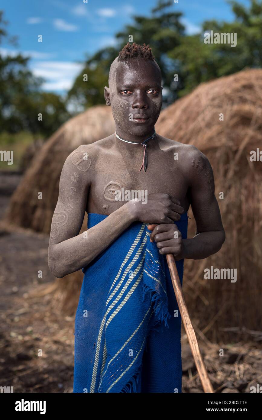 Con cicatrici ornamentali e personale di camminata, un giovane della tribù Mursi o gruppo etnico, Olikoru Village, Jenka, Etiopia. Foto Stock