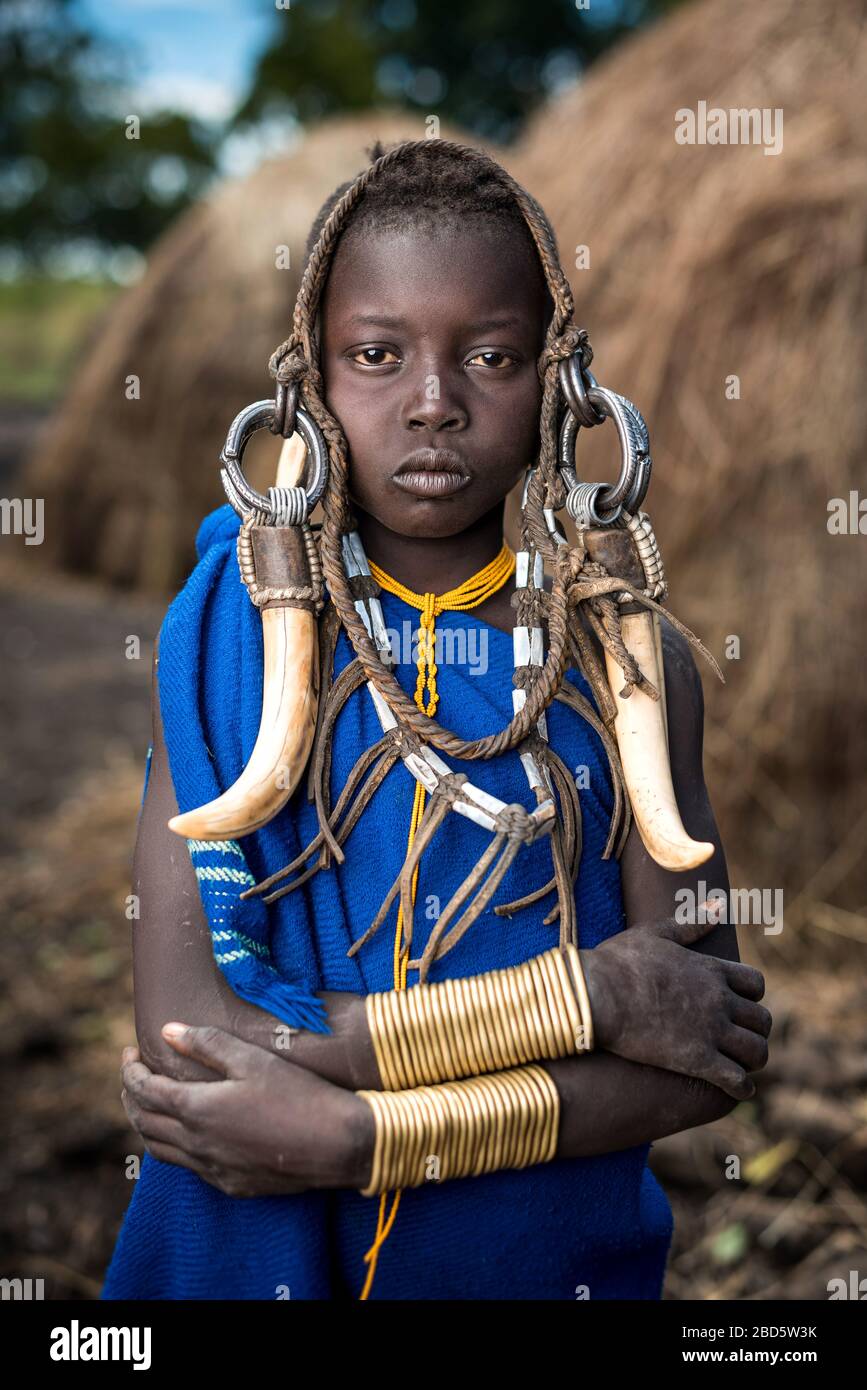 Una giovane ragazza si adorna di corno di bestiame, pelletteria e gioielli in metallo, tribù Mursi o gruppo etnico, Olikoru Village, Jenka, Etiopia. Foto Stock