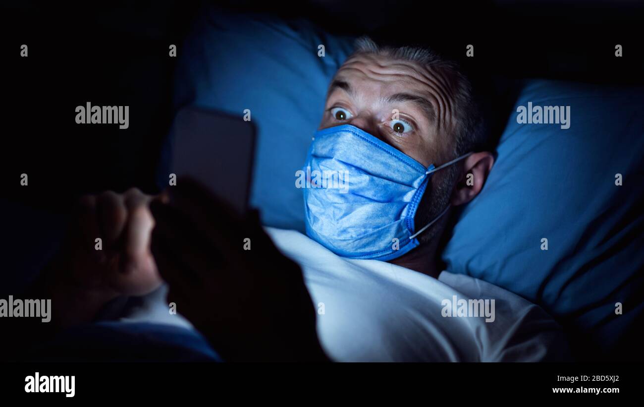 Uomo che usa smartphone leggere le notizie di Coronavirus che giacciono nel letto, Panorama Foto Stock
