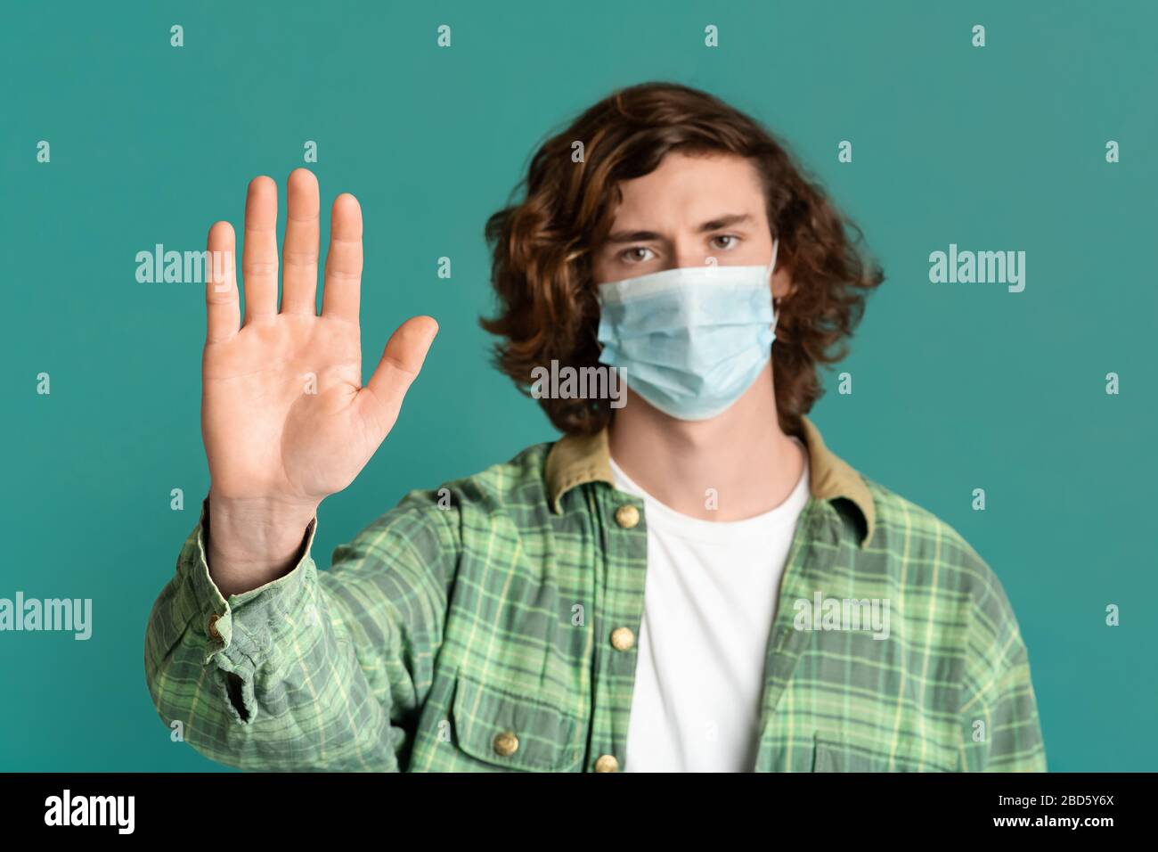 Giovane ragazzo che indossa la maschera medica e mostra IL gesto STOP, sfondo turchese Foto Stock
