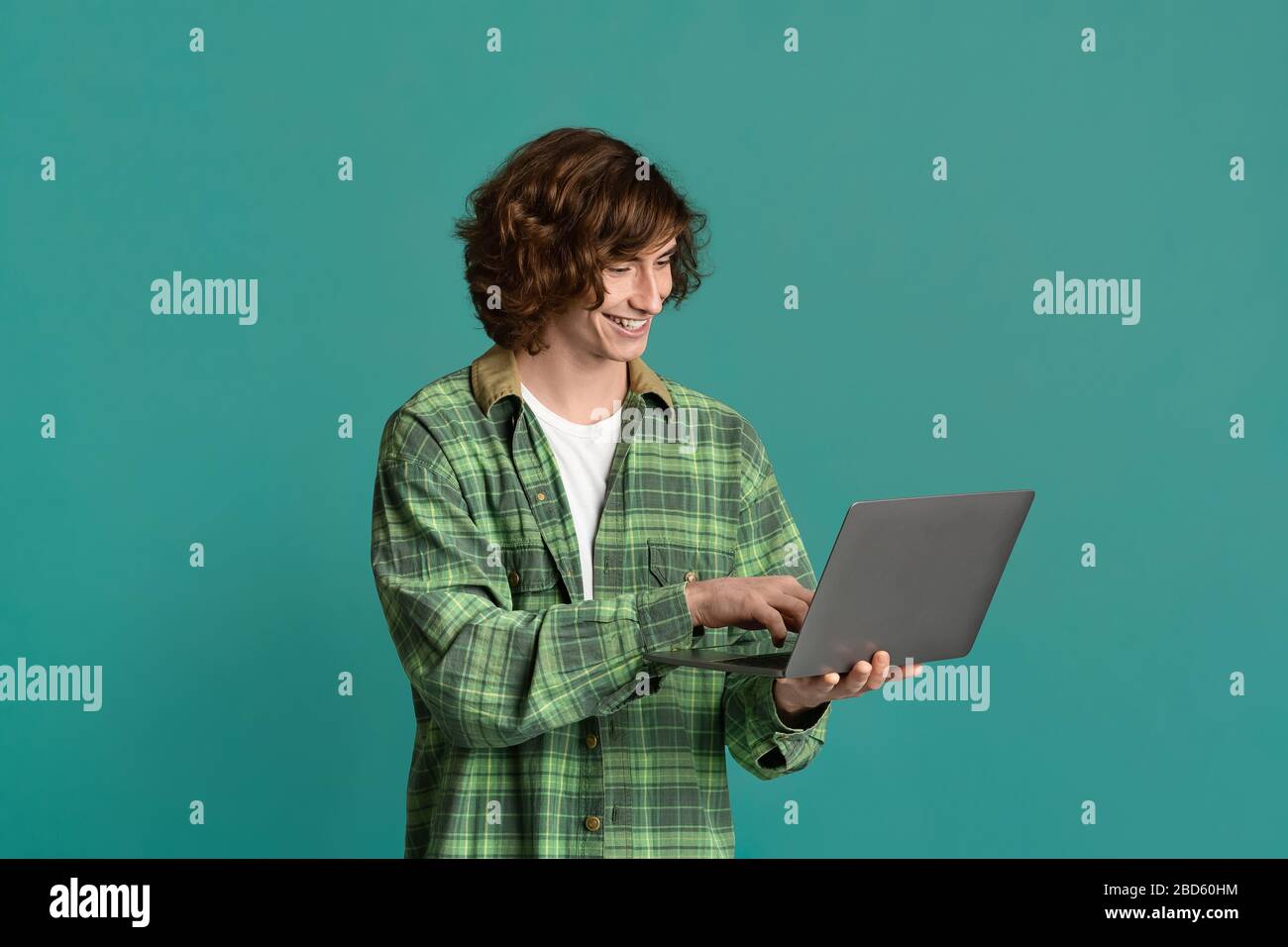 Comunicazione remota. Bel ragazzo giovane con notebook che chiacchiera online, lavora o studia su sfondo a colori Foto Stock
