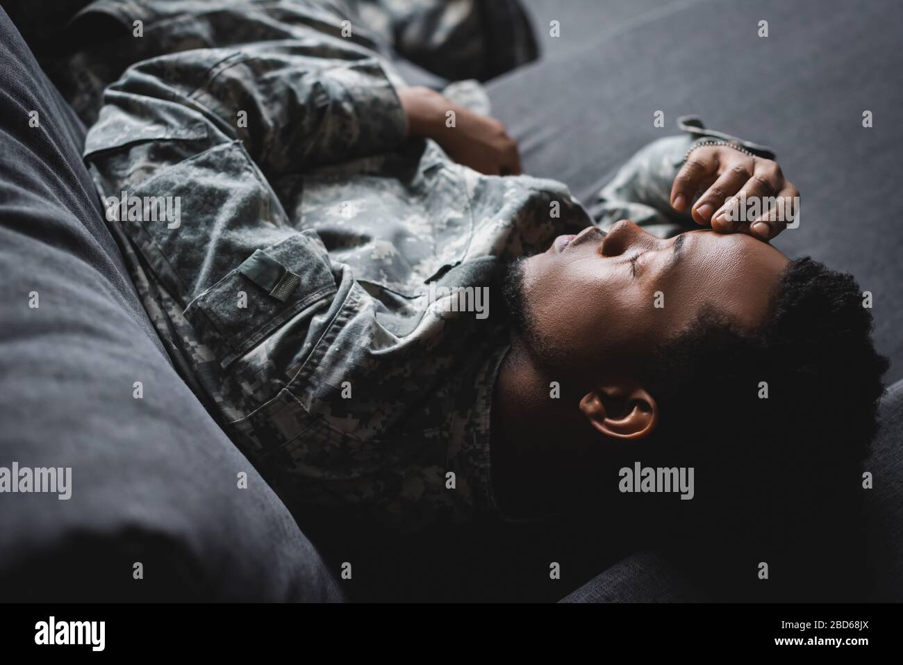 stanco soldato afro-americano in uniforme militare che dorme in divano a casa Foto Stock