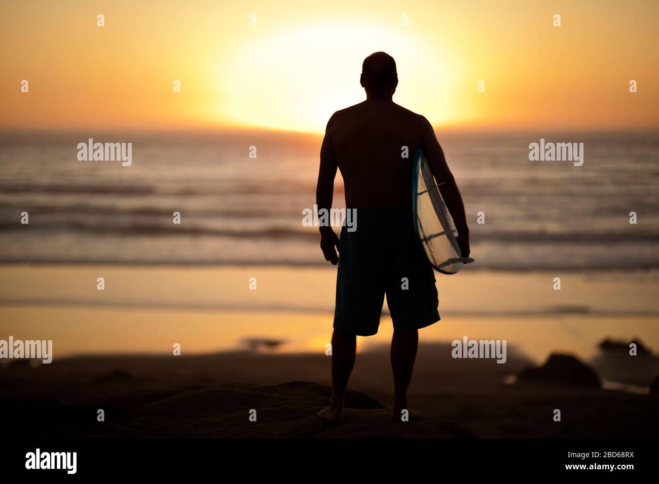 Silhouette di un uomo con la sua tavola da surf, guardando verso il mare. Foto Stock