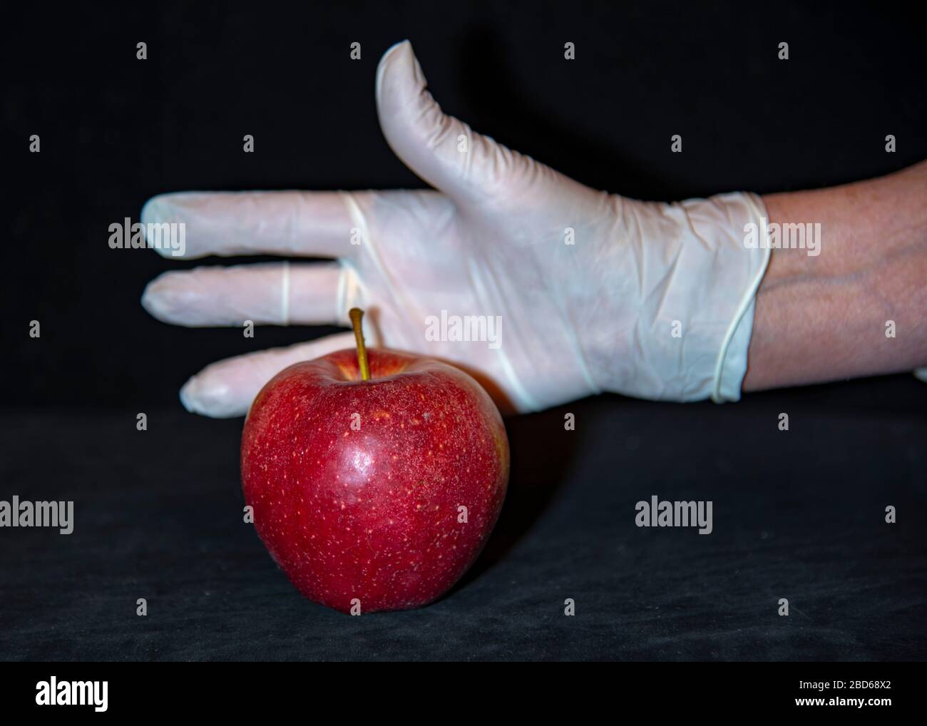 Una mano di donna in un guanto di gomma e una mela rossa . Foto Stock