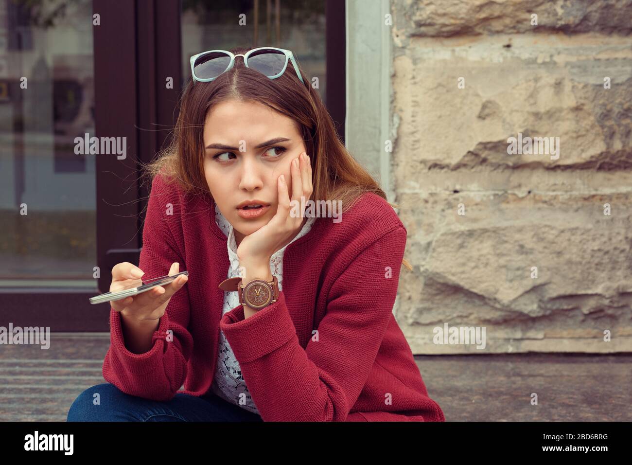 Ragazza triste in attesa di una chiamata o di un messaggio cellulare da parte del suo ragazzo seduto in una panchina all'aperto in strada con uno sfondo urbano Foto Stock