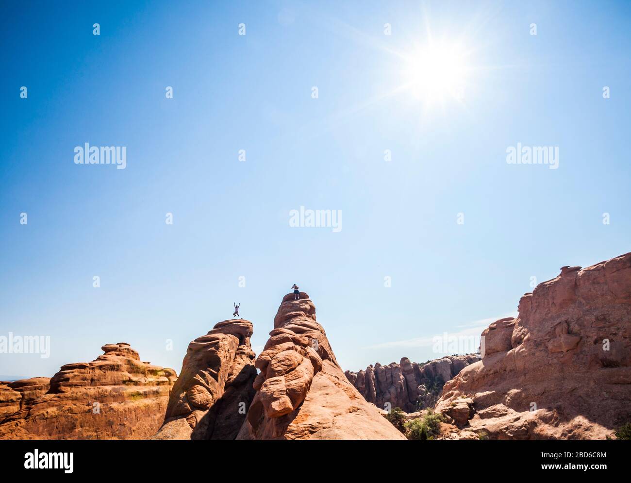 Un uomo che salta per la gioia sopra una pinna di arenaria nel Parco Nazionale di Arches mentre il suo amico scatta la sua foto. Utah, Stati Uniti. Foto Stock