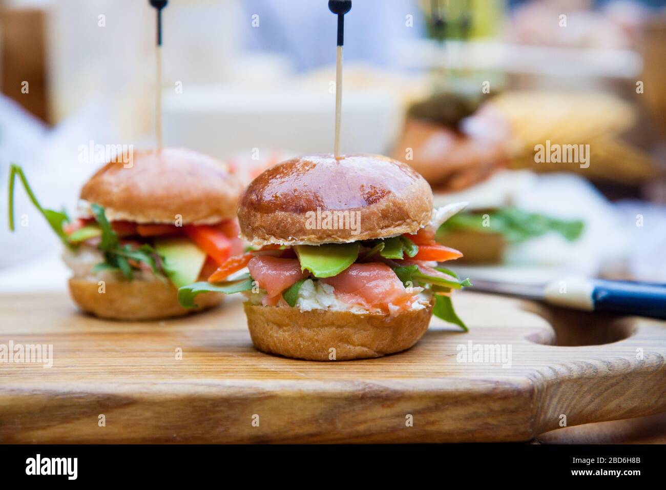 Hamburger con formaggio spalmabile, salmone salato, cale, avocado su panino di grano. Sfondo rustico. Foto Stock