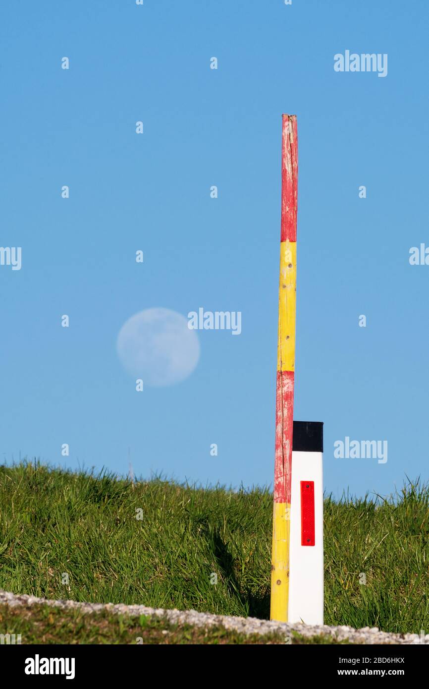 Indicatore di bordo riflettente e asta della neve sul lato della strada con luna in salita sullo sfondo. Traffico, segnali e segnaletica, segnaletica stradale e sicurezza Foto Stock