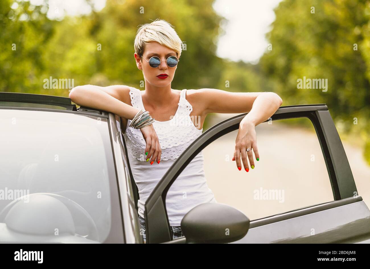 Giovane bionda attraente donna è pronta ad entrare nella sua auto. Sta aprendo la porta e rimanendo dietro di essa. Foto Stock