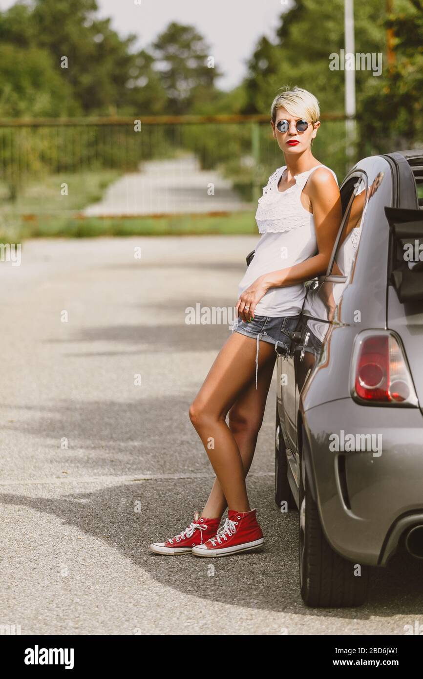 Giovane donna piuttosto alla moda che posa su un'auto. Concetto di stile di vita giovane. Foto Stock