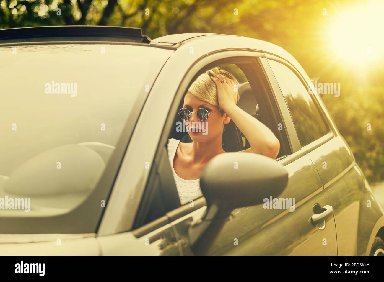 Giovane bionda attraente donna sorridente e guardando dritto mentre guida una macchina. Foto Stock