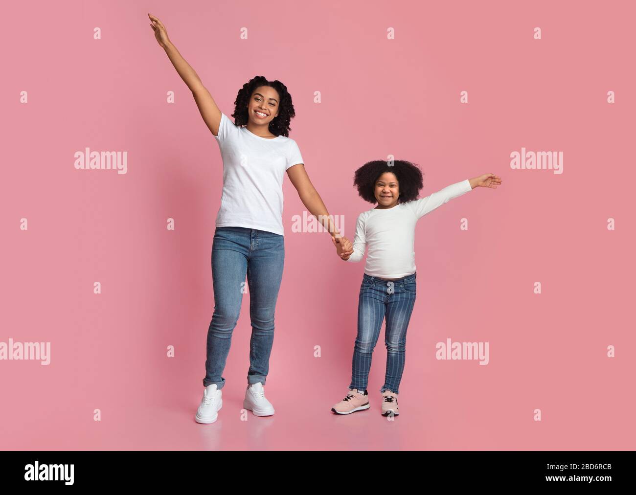 Felice mamma e figlia nera sorridente che posano con le mani sollevate Foto Stock