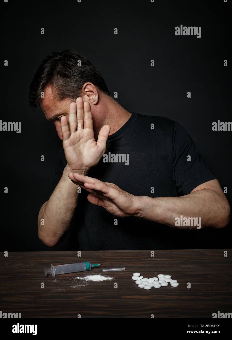 L'uomo in disperazione dalla tossicodipendenza è seduto a un tavolo Foto Stock