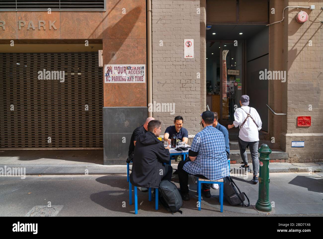 Melbourne, Australia - Marzo 9 2020; gruppo di uomini seduti intorno al tavolo del caffè nella strada posteriore della città discutendo questioni di interesse mentre il cameriere cammina Foto Stock
