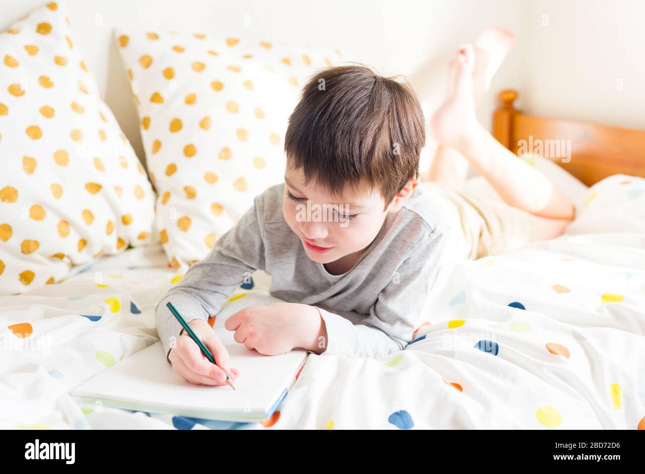 School Boy a letto e fare scuola a casa, scrivere in notebook. Formazione a distanza online. Quarantena. Concetto di soggiorno a casa Foto Stock
