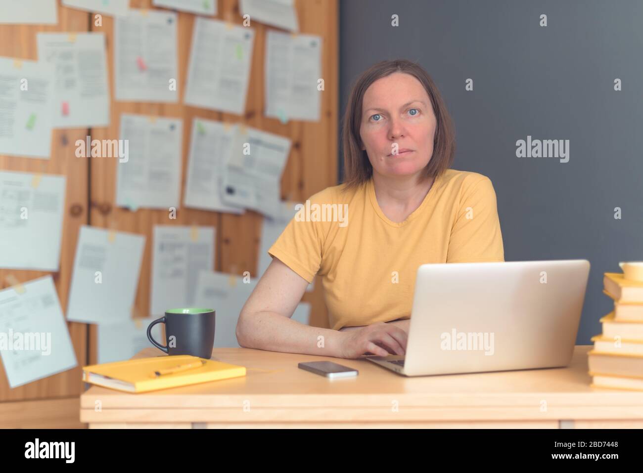 Traduttore freelance femminile attento che lavora in ufficio con computer portatile e smartphone, con un'attenzione selettiva Foto Stock