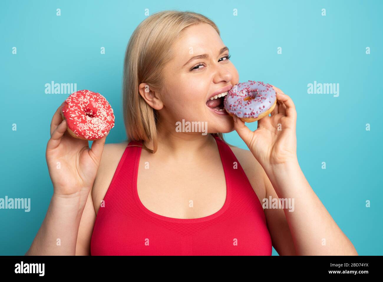 La ragazza grassa mangia dolce invece di fare palestra. Sfondo ciano Foto Stock