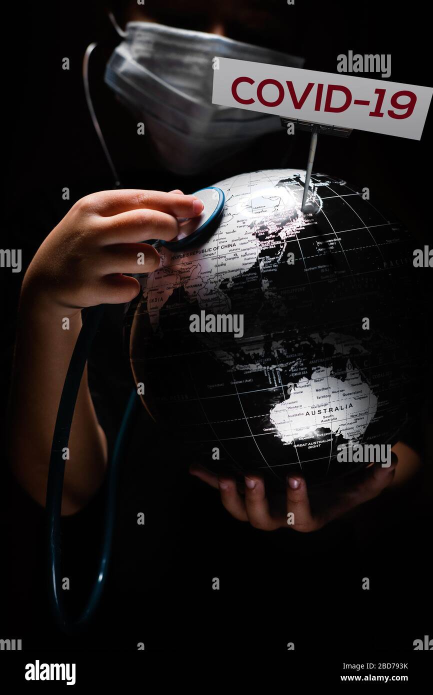 Kid Hold Globe mettere stetoscopio sulla sfera dove mostrato segno COVID-19 lettere rosse, faccia coperta in maschera su sfondo nero. Diffusione globale pandemica inf Foto Stock
