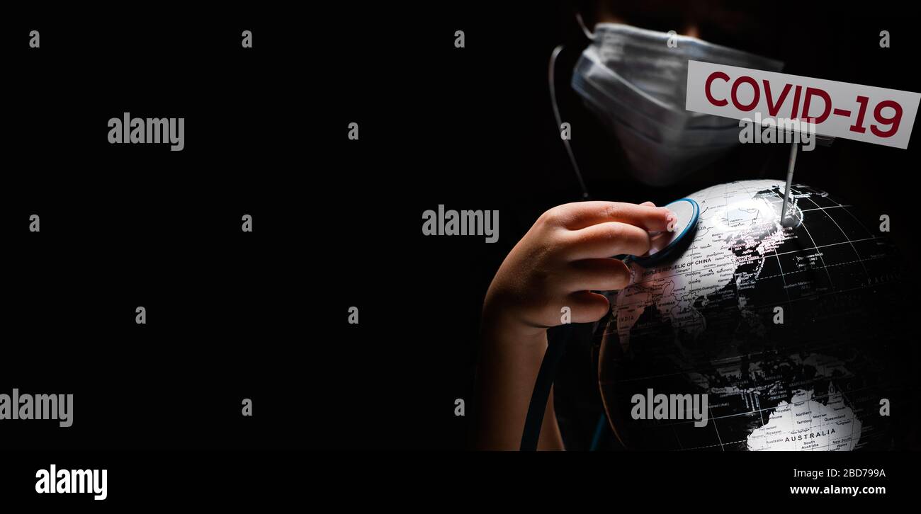 Kid Hold Globe mettere stetoscopio sulla sfera dove mostrato segno COVID-19 lettere rosse, faccia coperta in maschera su sfondo nero. Diffusione globale pandemica inf Foto Stock