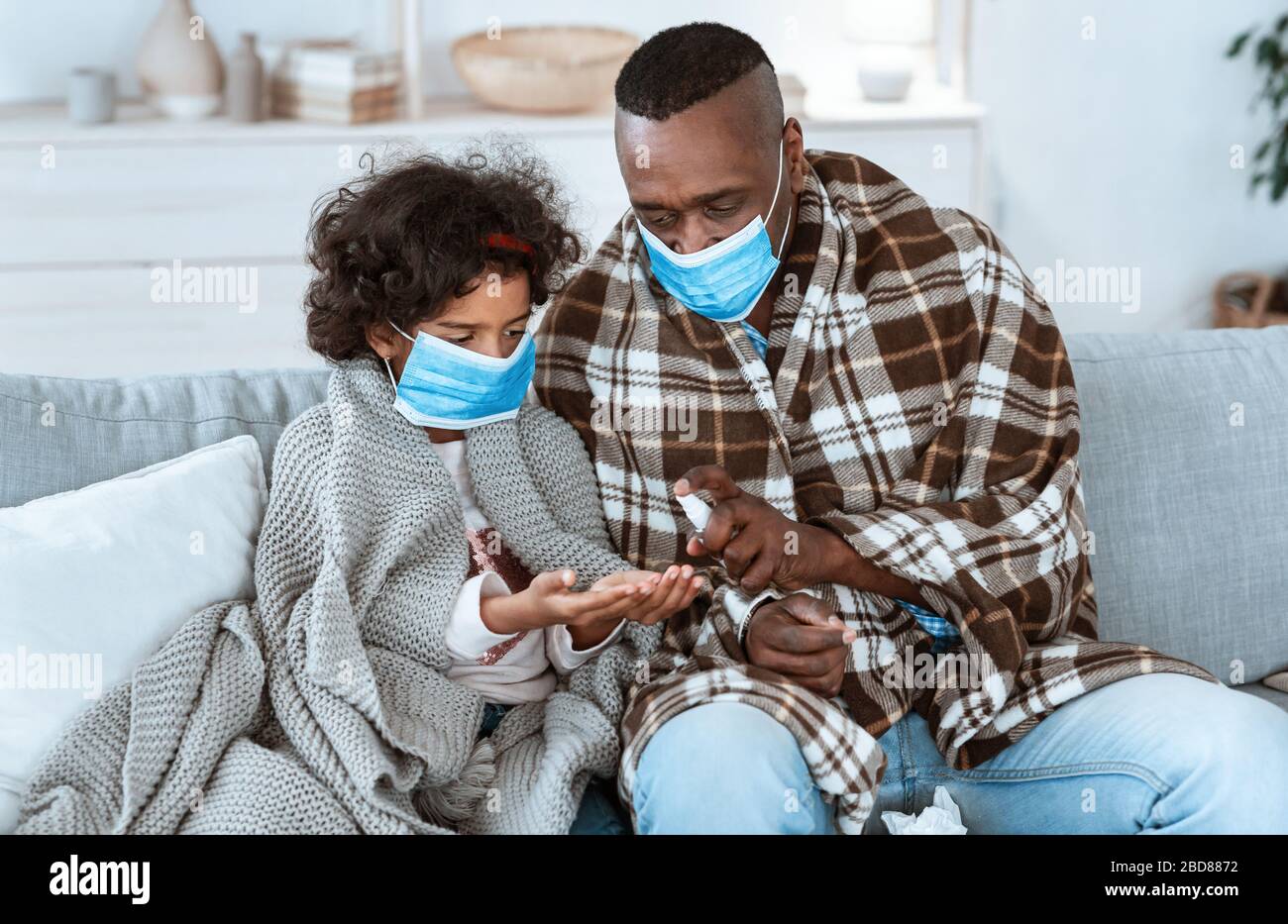 Strategie di igiene epidemica. Famiglia Afro-americana che indossa maschere protettive e mani di pulizia con igienizzatore al chiuso Foto Stock