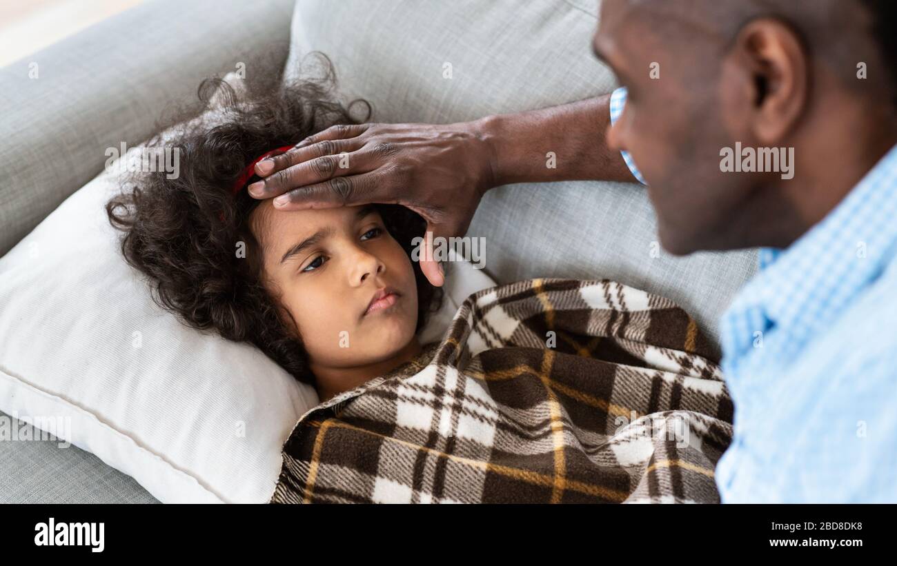 Epidemia di virus. Uomo africano americano anziano che tocca la fronte di sua nipote, controllando la febbre a casa Foto Stock