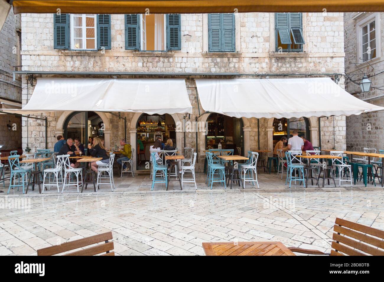 Caffè con tende sul marciapiede, la città vecchia di Dubrovnik, con un cameriere che serve alcuni clienti. Foto Stock