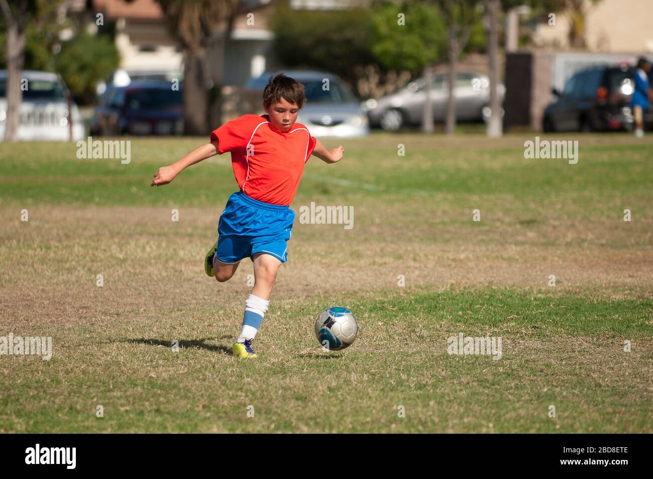 Giovane giocatore di calcio in uniforme rossa blu calcio palla nel parco Foto Stock