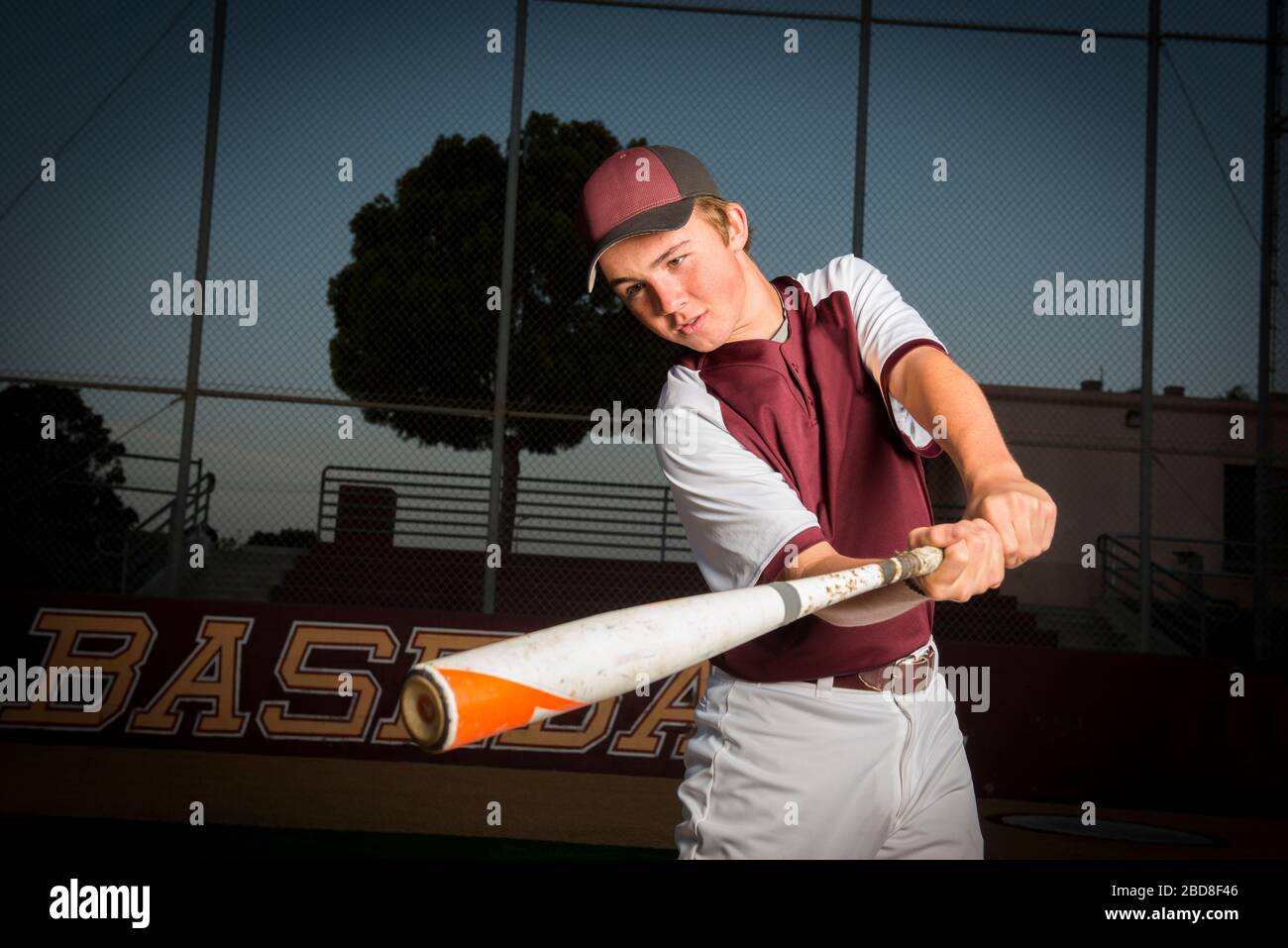 Ritratto di un giocatore di baseball High School in uniforme di maroon oscillare il suo pipistrello Foto Stock