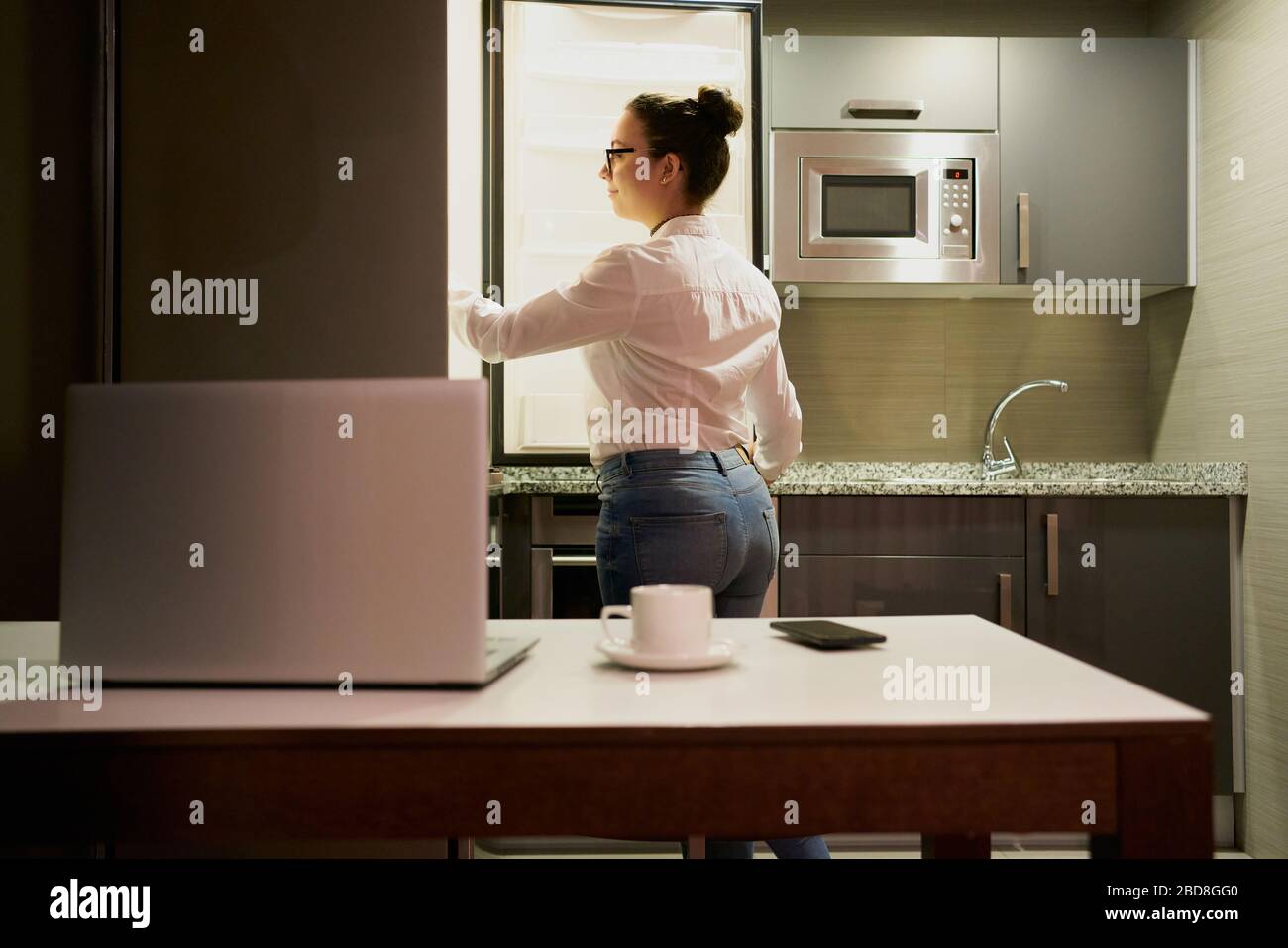 Una giovane donna che lavora con un notebook guarda nel frigorifero Foto Stock